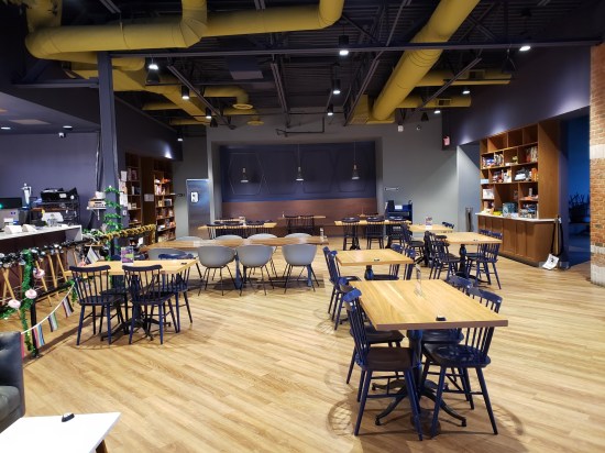 Dining room with beautiful hardwood floor, industrial-chic ceiling above Day-Glo painted pipes, and two cabinets of board games on opposite walls.