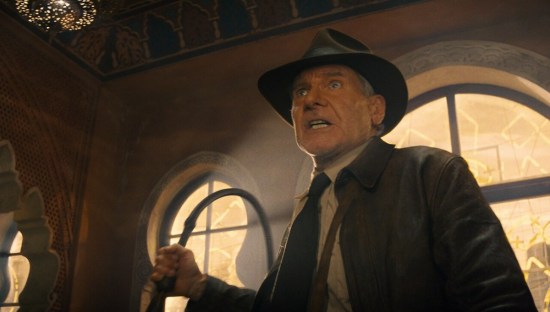 Angry Indiana Jones standing indoors and brandishing his whip.