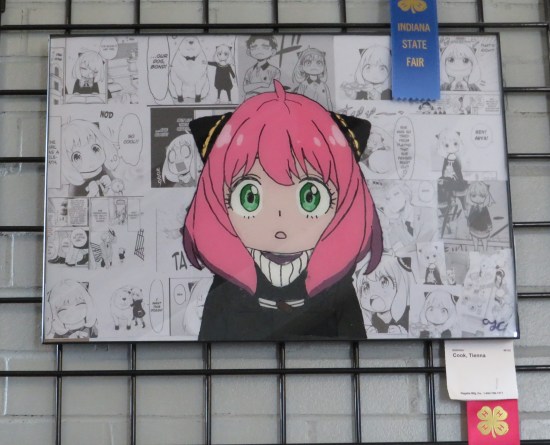 A pink-haired manga-style girl in a black robe. Behind her is a collage of black-and-white panels from her manga "Spy x Family".