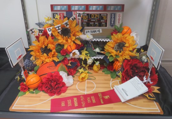 A diorama of a high school gym with basketball nets, covered in orange flowers.