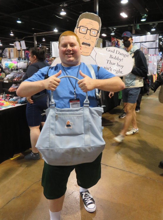 Bobby Hill carrying a sign that makes it look like Hank Hill is yelling at him over his shoulder.
