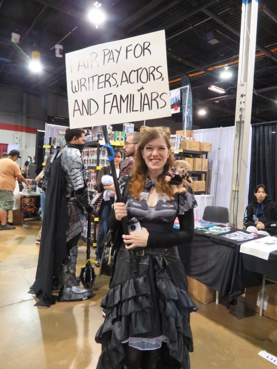 Fantasy cosplayer carrying a picket sign reading, "Fair Pay for Actors, Writers, and Familiars".