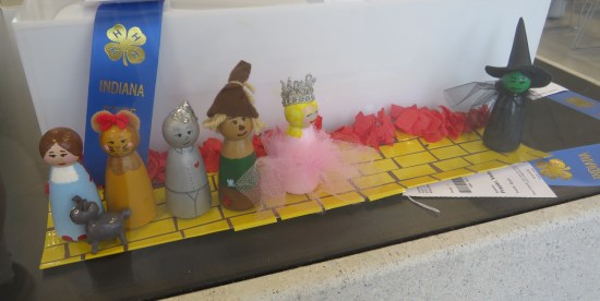 Imitation Fisher Price figures of the main cast of "The Wizard of Oz" on a paper strip colored like The Yellow Brick Road.