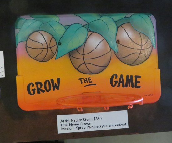 Custom-painted backboard labeled "Grow the Game" with basketballs growing on a tree.