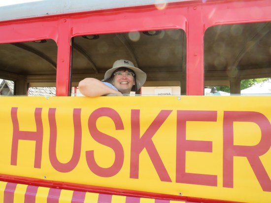 A smiling Anne sitting aboard that same bus, with only the "HUSKER" part of the sign in frame.