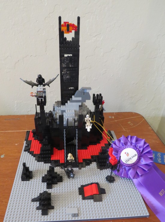 A Lego Sauron from "Lord of the Rings" looms over a Mordor gate with three evil characters coming out.