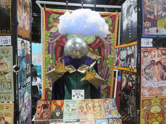 Mysterio in an Artists Alley booth surrounded by art, with a cotton cloud hanging over his head.