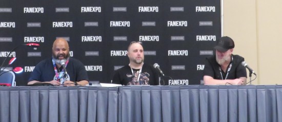 Our moderator and two comics artists sitting at a table on a platform at the front of a small convention ballroom.