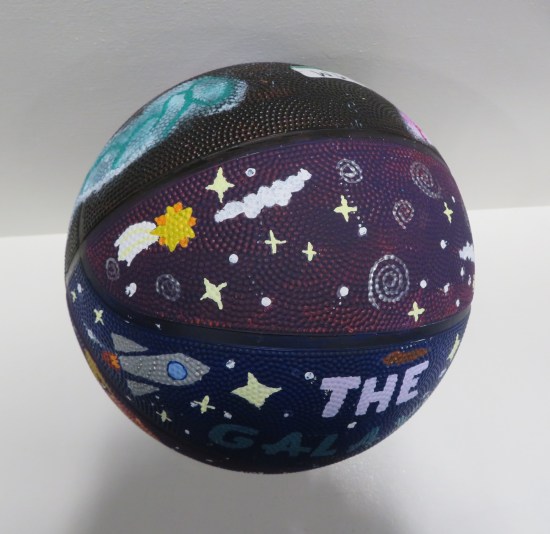 A black-and-purple basketball decorated with stars, nebulae, a sun, and a rocketship.