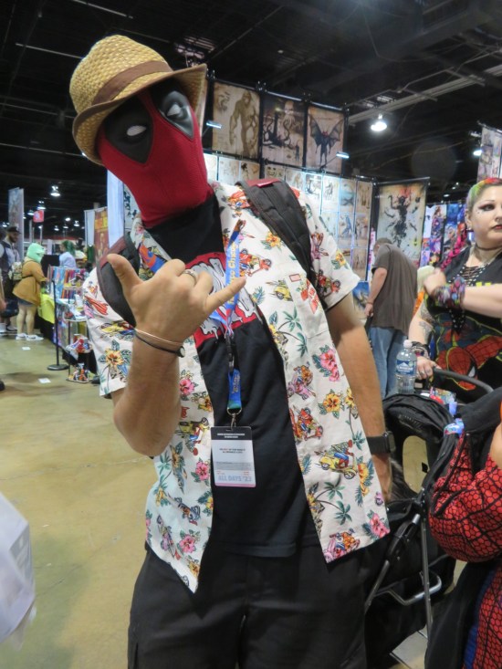 Deadpool with Hawaiian shirt and straw hat, throwing up a rockin' devil-horn gesture.