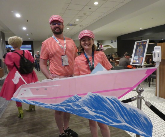 cosplay: Barbie and Ken in matching pink striped shirts, holding up a cardboard Barbie Boat facade.