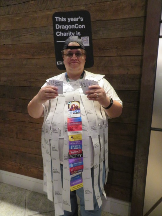 A guy wearing hundreds of Cards Against Humanity fastened into a robe. He's also holding cards toward us.