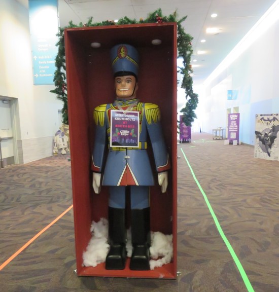 A large wooden toy soldier in a red box. A paper hung on its chest advertises David Krumholtz's autograph booth.
