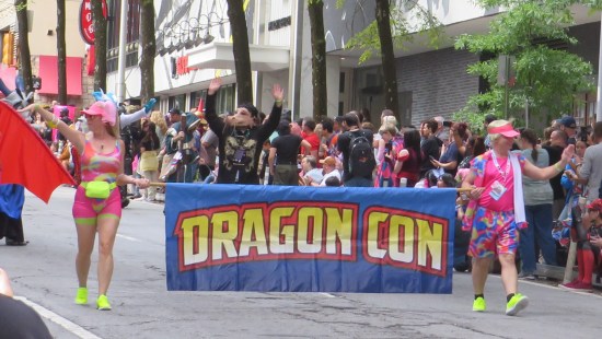 Barbie & Ken cosplayers carry the Dragon Con banner down the street.