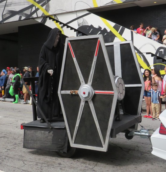 Emperor Palpatine rides a trailer with a TIE Fighter model about his height.