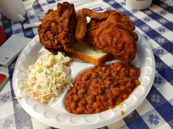 Hot fried chicken on a paper plate with baked beans and potato salad.