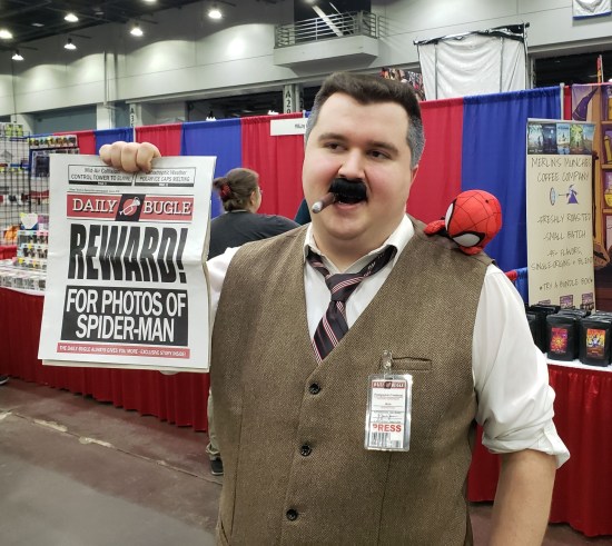 cosplay: J. Jonah Jameson with cigar in mouth, Daily Bugle newspaper offering rewards for Spider-Man photos, and a press pass clipped to his tweed vest. A tiny stuff Spidey is sewn to his shoulder.