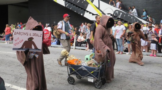 Jawa pulling a wagon with a skeleton and a stuffed Grogu; Jawa with Mjolnir; Jawa with a picket sign: "Bargins & Dealz: Not Stolen!"