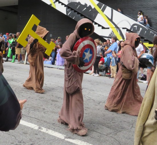 Three Jawas carrying random objects: Captain America's shield, a giant letter T, and a Jango Fett helmet.