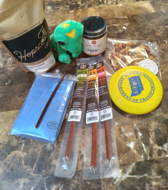 On our kitchen table at home: a stuffed GEICO gecko, a small yellow Indiana Department of Transportation frisbee, three strips of duck jerky, a chocolate chip cookie, a bag of coffee beans, and a jar of za'atar.