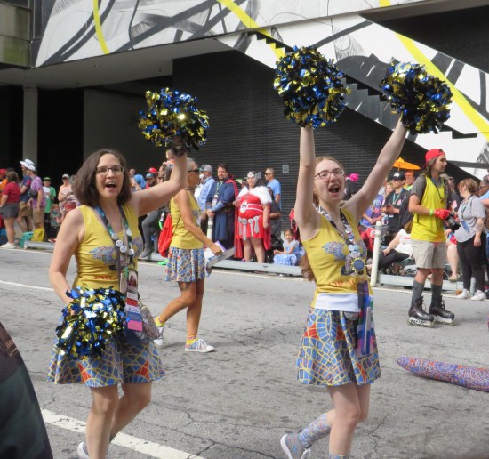 two cheerleaders in Marriott Carpet-patterned skirts and yellow tops. Their pom-poms are appropriately blue and gold.