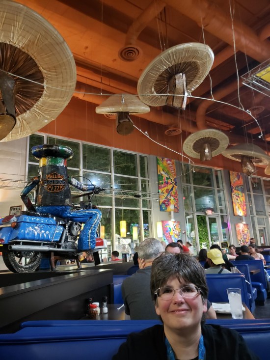 Anne sitting below a restaurant ceiling with giant fake mushrooms dangling from it.