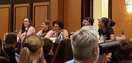 five panelists poorly photographed from a distance in a ballroom with unfavorable lighting.