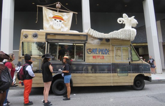 A food truck with "One Piece" decor all over it. Of the four visible customers, three wear hats.