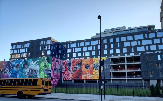 A colorful mural on a building that's parking garage for the first four floors and something with glass windows for the top four.