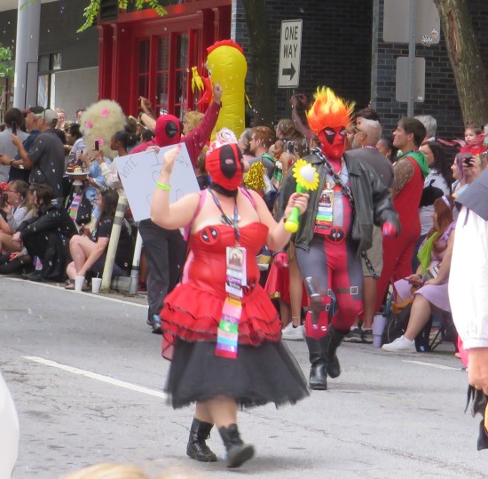 Woman in Deadpool mask, strapless short red dress, longer black skirt underneath, tiara and battery-powered sunflower fan.