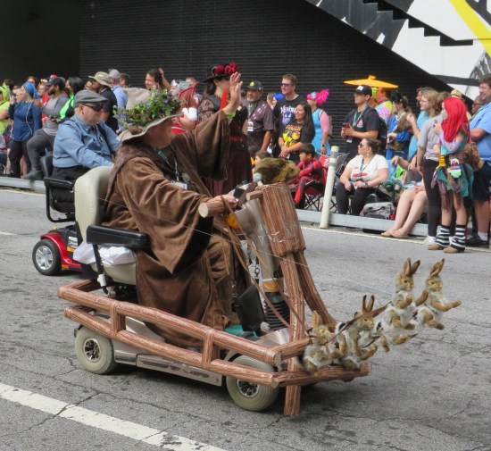 Radagast cosplayer rides a brown mobility scooter with woodsy details. Four stuffed bunnies hang from a bow on the front, kinda like Santa's reindeer.