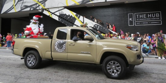 Evil Robot Santa in the back of a beige pickup truck with the Planet Express logo on the door and a small inflatable Hypnotoad on the roof.
