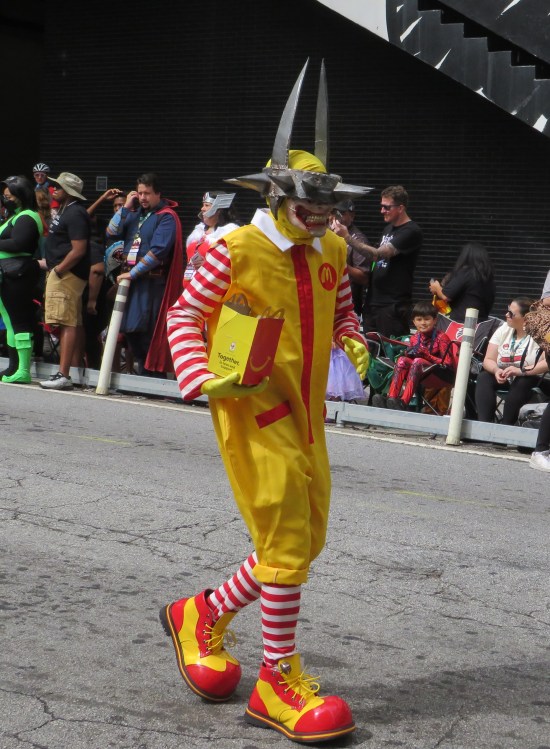 Ronald McDonald wearing a spiked iron ring around his eye with two more spikes jutting upward Batman-style. He carries an open Happy Meal box.