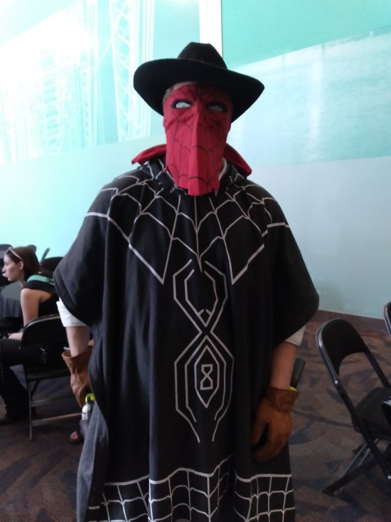 cosplay: black-clad cowboy with Spider-Man bandanna on his face and red gloves.