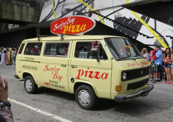 Yellow Surfer Boy Pizza van with red sign on top. A Demogorgon puppet hangs from the front passenger window.