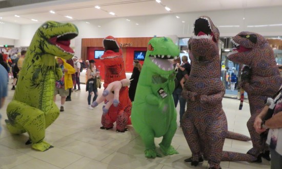 five inflatable tyrannosaurus Rex costumes: one green, one Reptar, two Marriott Marquis carpet skinned, and one red holding a limp stuffed unicorn.