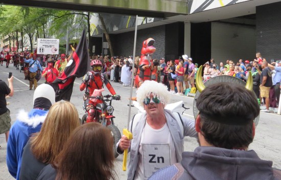 Dude in a white jacket, wig, and shirt with a plastic sword and zinc's periodic table entry on his chest wades into the crowd.  Behind him Deadpools are coming!