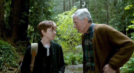 A short-haired Elsie Fisher and a slightly hunched, shabbily dressed Stephen Lang converse in the woods.