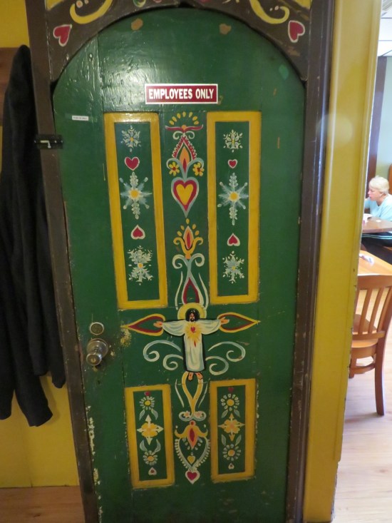 A green Employees Only door with yellow German-esque trim and a small Catholic Jesus painted in the middle.