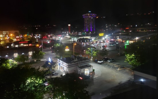 Nighttime view of a working-class neighborhood with a McDonald's, White Castle, a Waffle House, and a tall, cylindrical, purple-lit Radisson hotel in the distance.