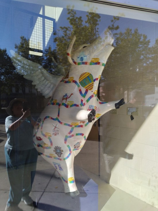 Statue of a flying pig, photographed from outside through the  front window. A Candy Land trail is painted all over the statue, leading to various forms of transportation as points of interest -- e.g., camel, hot-air balloon, etc.