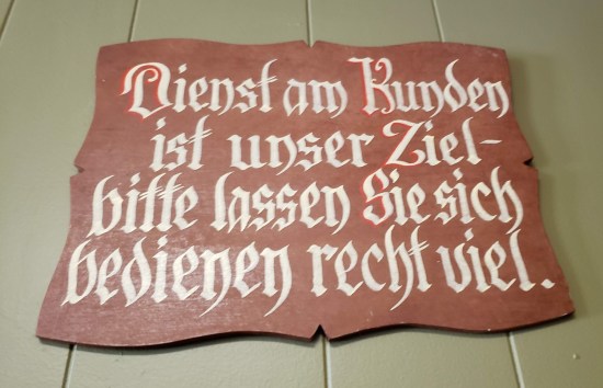 Wooden sign in German: "Dienst am Kunden ist unser Ziel Bitte lassen Sie sich bedienen recht viel."