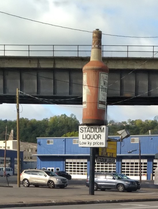 A giant brown bottle of Wild Turkey whiskey on a pole in front of a store called Stadium Liquor, whose sign boasts "low Kentucky prices".