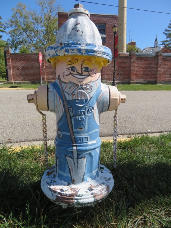 Fire hydrant painted like a blond man wearing overalls and a blue shirt with red vertical lines.