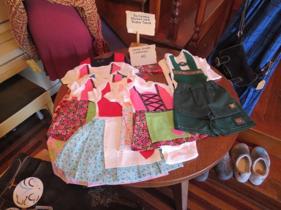 A round oak table with one pair of boys' lederhosen and several German girls' dresses.
