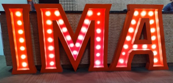Large red theater-sign letters "IMA" with clearly visible white light bulbs, mounted on the front of a bar.