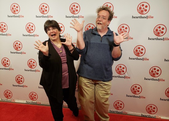 Me and Anne doing jazz hands on a red carpet. The wall behind us is covered in Heartland International Film Festival logos, red on white. Anne is dressed much nicer than I am, but I tried.