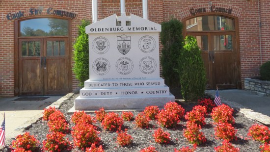 A large Greco-Roman tombstone in a mulched lawn. It bears the town crest, the seals of each of America's five Armed Forces, and an inscription marking its 2012 dedication and the town's 175th anniversary. At the bottom it reads, "Dedicated to those who served: God, Duty, Honor, Country".