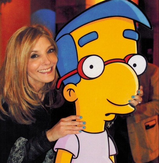 Pamela Hayden smiling while holding on to a large cardboard standee of Milhouse, who looks confused as usual.