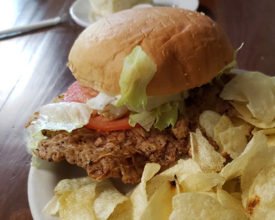 Closeup of a pork tenderloin sandwich plated with ordinary potato chips.
